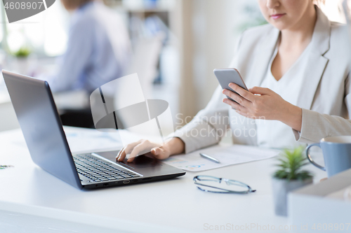 Image of businesswoman with smartphone and laptop at office