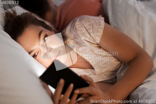 Image of woman using smartphone while boyfriend is sleeping