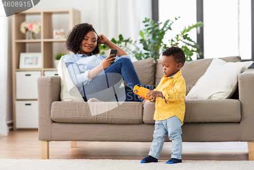 Image of baby playing toy car and mother with smartphone