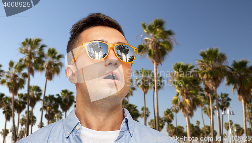 Image of surprised man in sunglasses over palm trees