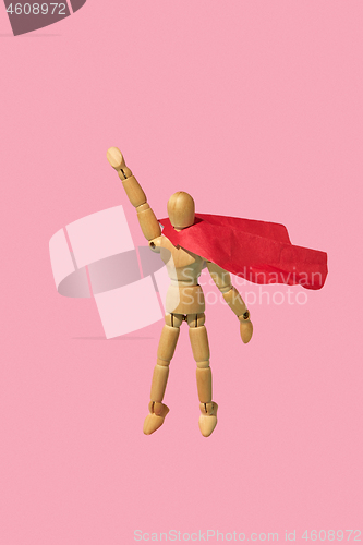 Image of Wooden mannequin miniature doll in a red cape flies up as a superman.