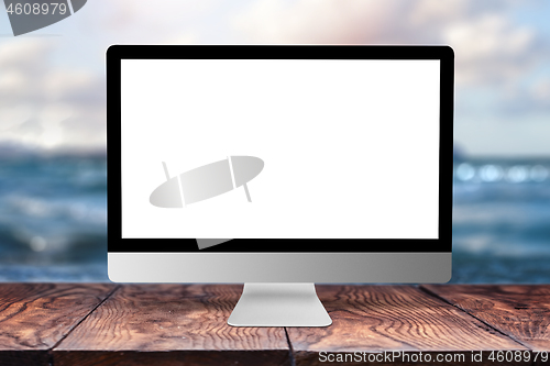 Image of Mock-up computer display on wooden table against sea background.