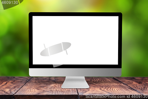 Image of Mockup computer screen on wooden table against a blurred background.