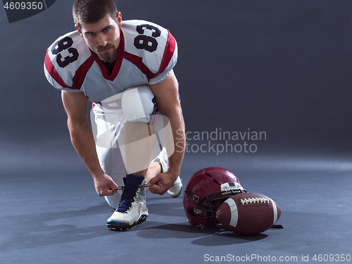 Image of American Football Player tie his shoe laces isolated on gray