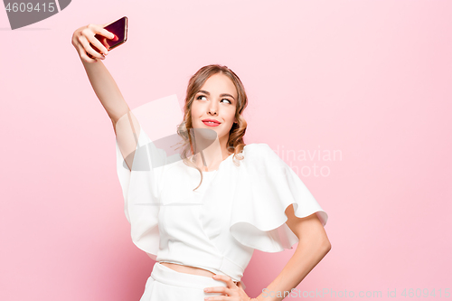 Image of Portrait of a young attractive woman making selfie photo with smartphone on a pink background