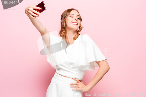 Image of Portrait of a happy smiling casual girl showing blank screen mobile phone isolated over pink background