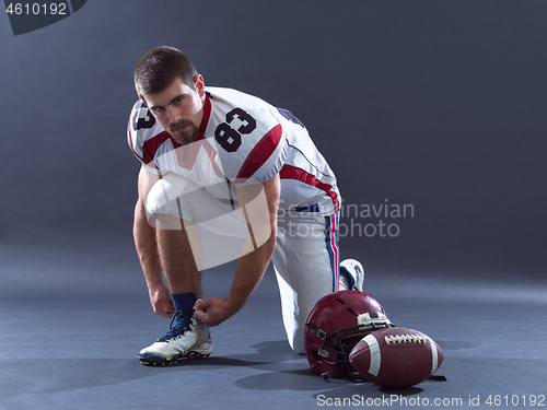 Image of American Football Player tie his shoe laces isolated on gray