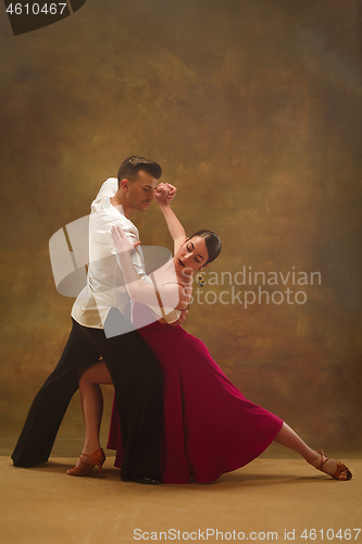 Image of Dance ballroom couple in gold dress dancing on studio background.