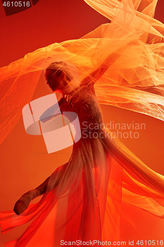 Image of Ballerina. Young graceful female ballet dancer dancing over red studio. Beauty of classic ballet.