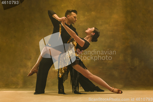 Image of Dance ballroom couple in gold dress dancing on studio background.