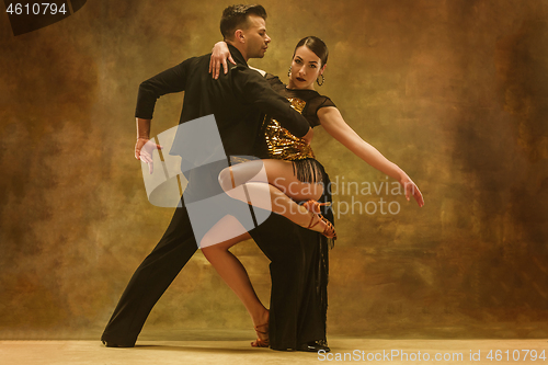 Image of Dance ballroom couple in gold dress dancing on studio background.