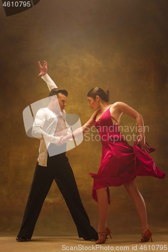 Image of Dance ballroom couple in gold dress dancing on studio background.