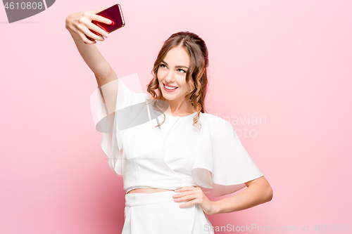 Image of Portrait of a young attractive woman making selfie photo with smartphone on a pink background