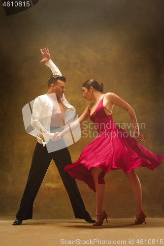 Image of Dance ballroom couple in gold dress dancing on studio background.