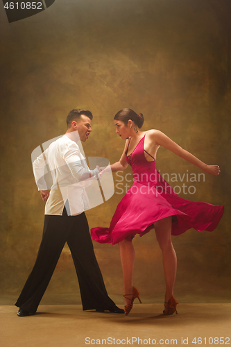 Image of Dance ballroom couple in gold dress dancing on studio background.