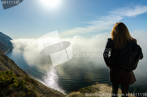 Image of Girl is watching from the mountain on an unusual seascape with clouds over the sea