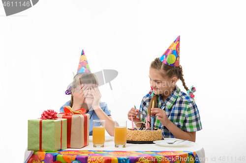 Image of One girl covered her eyes with her hands, the other inserts matches in a birthday cake