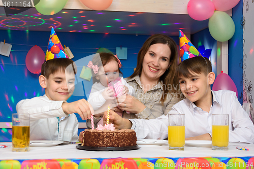 Image of Children on a family birthday put candles in a birthday cake