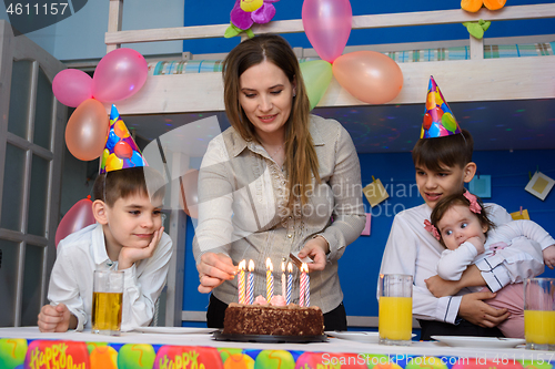 Image of Mom lights candles at a birthday celebration in the children\'s room, around the children