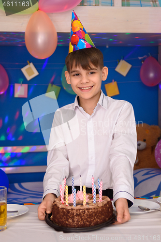 Image of A boy at his birthday stands at the table with a cake