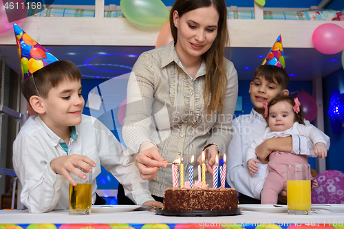 Image of Girl lights candles on a pie at the festive table