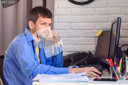 Image of Freelancer thoughtfully looks out the window, sitting at his workplace