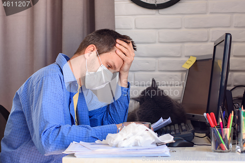 Image of A man in a protective medical mask sits at a computer in a home stop and reads documents