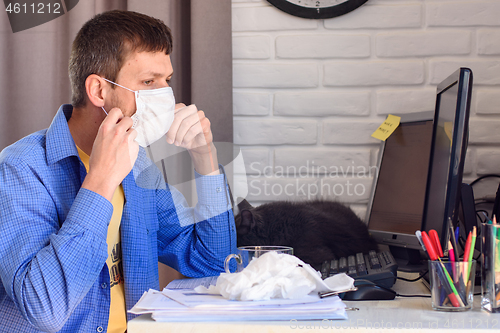 Image of A man puts on a protective medical mask while working at home at the computer