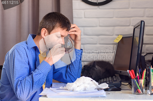 Image of A sick man sits at a computer and drinks tea