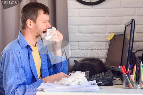 Image of Young man sneezes while at a computer