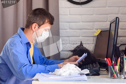 Image of A man in a medical mask reads a document while working remotely