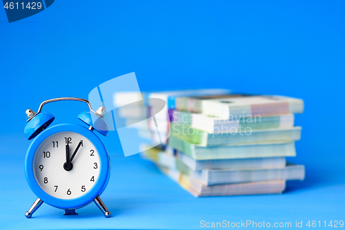 Image of In the foreground is an alarm clock, in the background is a stack of bills