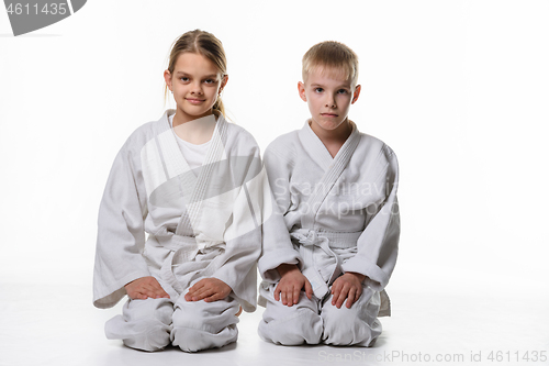 Image of Two judo students sit on their knees and look in the frame