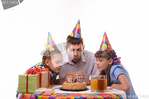 Image of Dad and two daughters together blow out the candles on the cake