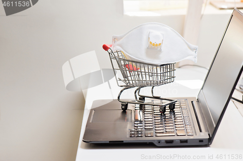 Image of Conceptual photo with miniature shopping-cart and protecting mask. Safety internet shopping