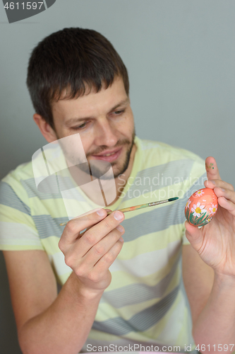 Image of Man paints an Easter egg with a brush