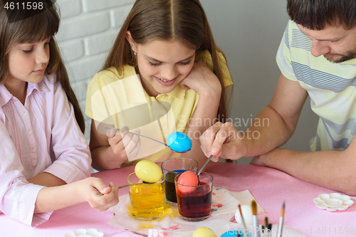 Image of Daddy paint eggs in glasses with colorful dyes.