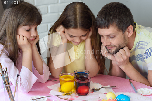 Image of Dad and two daughters are watching how the eggs are painted in glasses with dyes