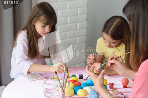 Image of Mom and daughters enthusiastically paint Easter eggs at home