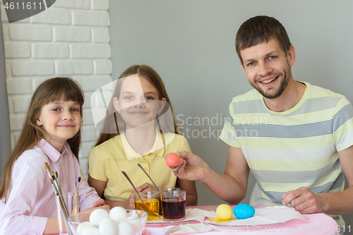 Image of Happy family paints easter eggs at the table and looked joyfully into the frame