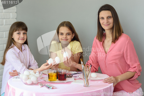 Image of Mom and two daughters are sitting at the table preparing eggs for Easter and looked in the frame