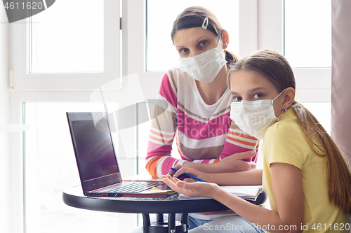 Image of Mom and girl in self-isolation mode are sitting at the table, doing homework and looked into the frame.