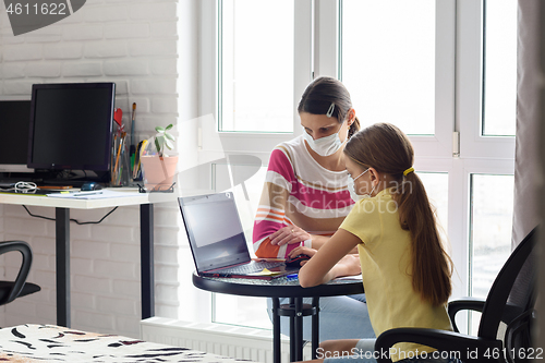 Image of Mom helps daughter do homework, both in medical protective masks