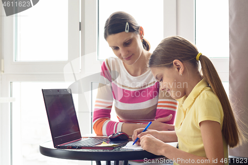 Image of A tutor teaches a child at home, a girl writes in a notebook