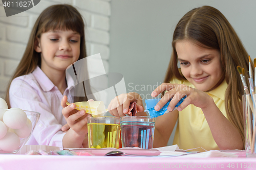 Image of Sisters pour dye for coloring eggs in a glass of water