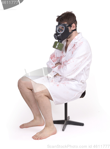 Image of Man wearing gas mask and bloody doctors coat sitting on small ch