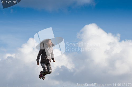 Image of Cute girl running jumping at the on a field in the summer