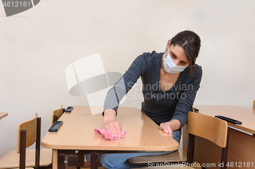 Image of Girl in a medical mask washes tables in a school class during the quarantine period