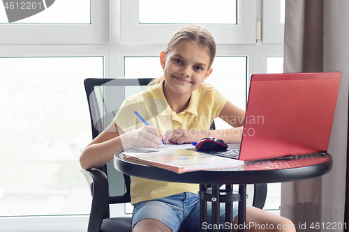 Image of The girl at the table at home does homework and looked into the frame.