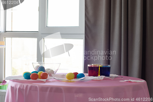 Image of Table with colorful Easter eggs and dyes in the interior of the room by the window